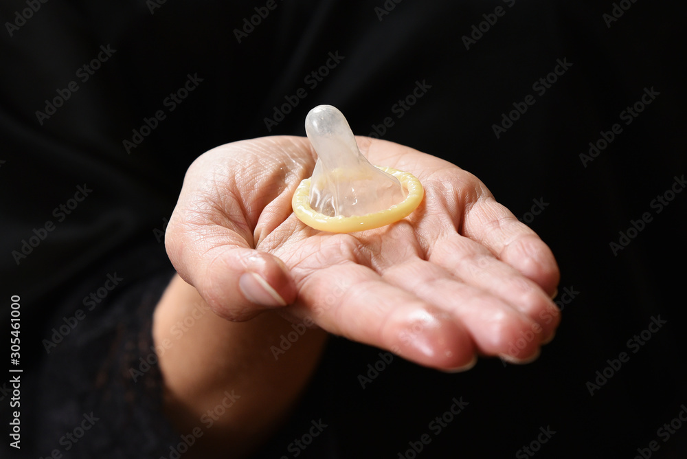 Condom in female hands on a black background close up. Condom in female hands on a black background close up.