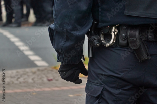 Belt of a policeman in black uniform in action, with handcuffs, baton and belt bag.