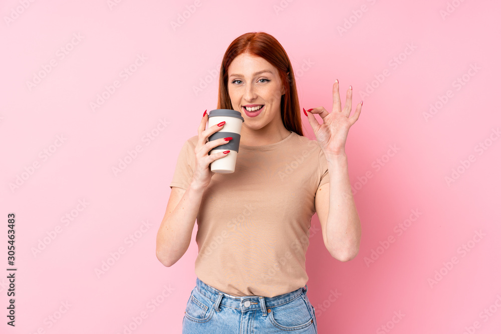 Young redhead woman over isolated pink background holding coffee to take away while making OK sign Young redhead woman over isolated pink background holding coffee to take away while making OK sign