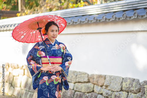 Geishas girl wearing Japanese kimono among red wooden Tori Gate at Fushimi Inari Shrine in Kyoto, Kimono is a Japanese traditional garment. The word "kimono", which actually means a "thing to wear"