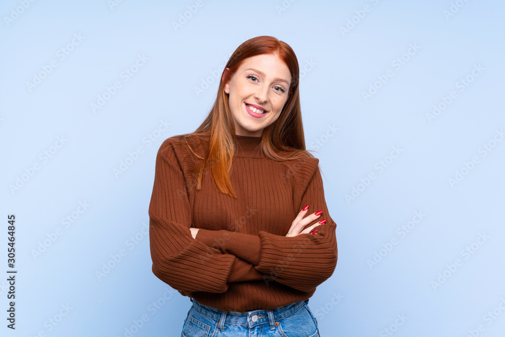 Young redhead woman over isolated blue background keeping the arms crossed in frontal position Young redhead woman over isolated blue background keeping the arms crossed in frontal position