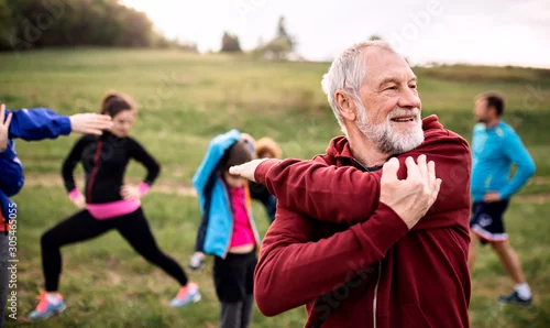 Obraz Duża grupa sprawnych i aktywnych osób wykonujących ćwiczenia w przyrodzie, rozciągających się.
