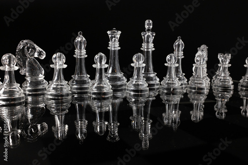 Transparent methacrylate chess pieces, front view placed on a reflective black surface