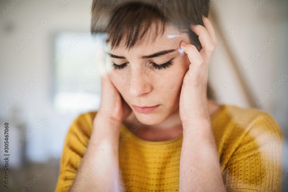 Front view of sad young woman standing indoors at home, close-up. Front view of sad young woman standing indoors at home, close-up.
