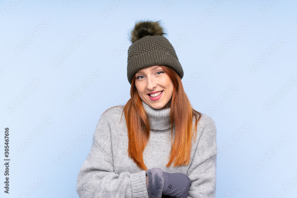 Young redhead Russian woman with winter hat over isolated blue background laughing Young redhead Russian woman with winter hat over isolated blue background laughing