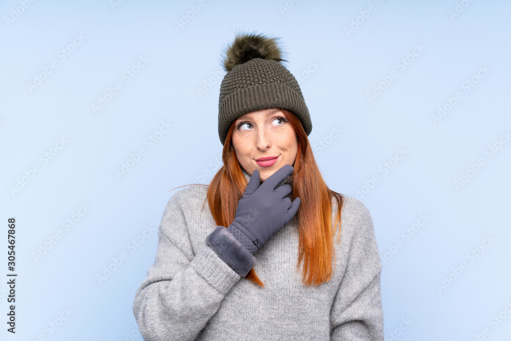 Young redhead Russian woman with winter hat over isolated blue background thinking an idea Young redhead Russian woman with winter hat over isolated blue background thinking an idea