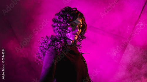 Young stylish curly woman in big sunglasses  moves to the music  taking off her headphones  dancing  against the wall.