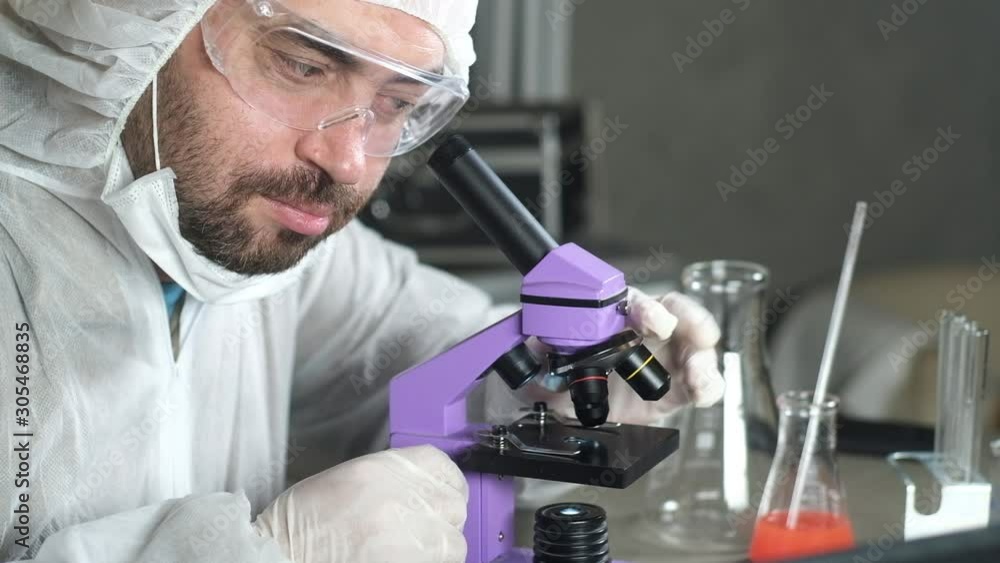 male scientist in laboratory looking through microscope and change magnification. Scientific discoveries in Microbiology or pharmacology. Research in laboratory. An experiment in a medical laboratory male scientist in laboratory looking through microscope and change magnification. Scientific discoveries in Microbiology or pharmacology. Research in laboratory. An experiment in a medical laboratory