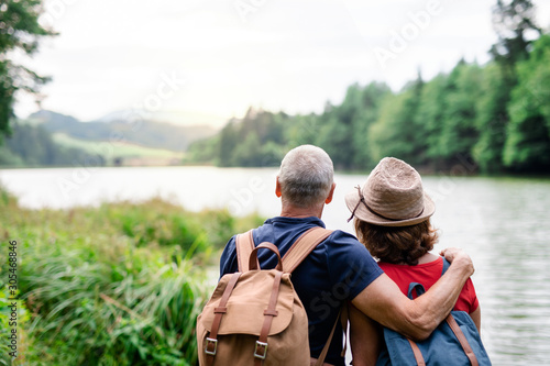 Rear view of senior tourist couple on a walk in nature, standing by lake. photo