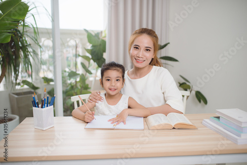 Asian mother and daughter doing home work together in living room