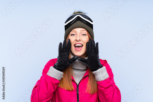 Skier redhead woman with snowboarding glasses over isolated blue wall shouting with mouth wide open