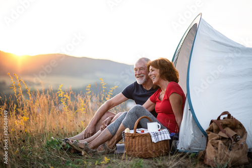 Senior tourist couple with picnic basket sitting in nature at sunset, resting. photo