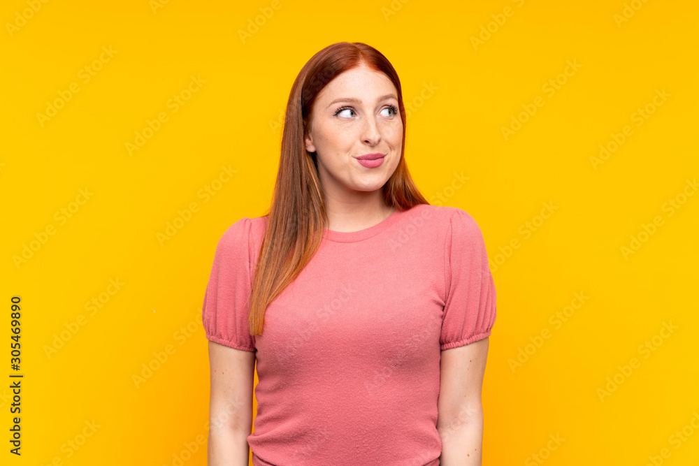 Obraz premium Young redhead woman over isolated yellow background standing and looking to the side