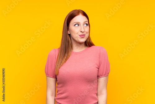 Young redhead woman over isolated yellow background standing and looking to the side