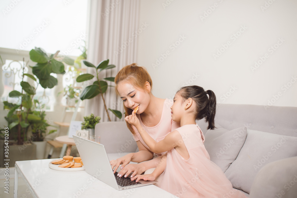 Young Asian beautiful mother teaching daughter using computer sitting on sofa at home. Young Asian beautiful mother teaching daughter using computer sitting on sofa at home.