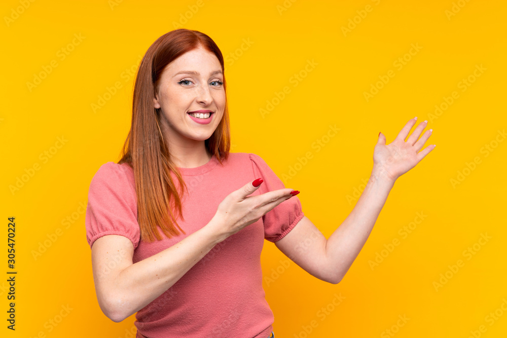 Young redhead woman over isolated yellow background extending hands to the side for inviting to come Young redhead woman over isolated yellow background extending hands to the side for inviting to come