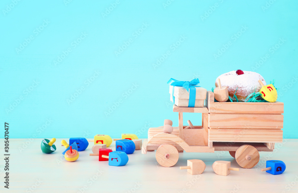 Obraz premium religion image of jewish holiday Hanukkah with spinning top and doughnut over wooden car toy and pastel blue background