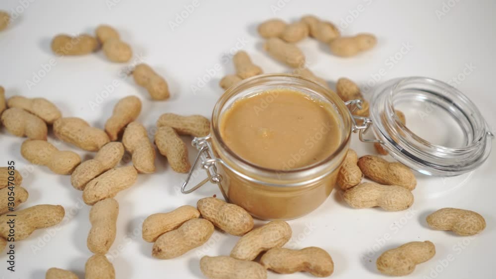 Peanut butter in a glass jar with a metal fastener on a white table close-up with a bunch of nuts. Healthy Organic Breakfast Peanut butter in a glass jar with a metal fastener on a white table close-up with a bunch of nuts. Healthy Organic Breakfast