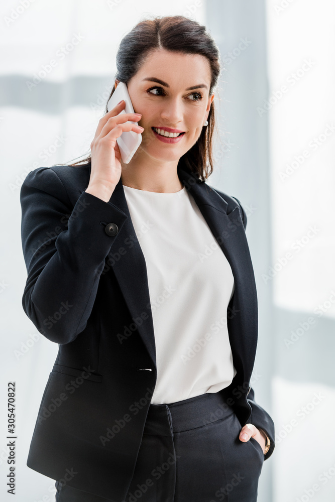 attractive diplomat standing with hand in pocket and smiling while talking on smartphone attractive diplomat standing with hand in pocket and smiling while talking on smartphone