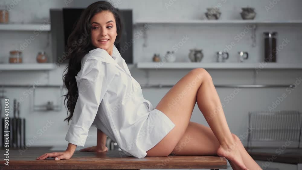 smiling woman sitting on table and stretching in kitchen smiling woman sitting on table and stretching in kitchen