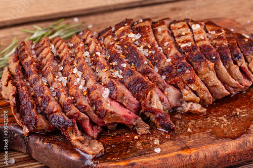 Close Up of Chopped Grilled Steak Rib Eye on Rustic Cutting Board on Wooden Background. Juicy Medium Ribeye Steak with Salt, Pepper and Rosemary. Concept of Delicious Meat Food