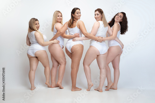 In love with myself. Portrait of beautiful plus size young women posing on white background. Happy smiling female models hugging. Concept of body positive, beauty, fashion, style, feminism. photo