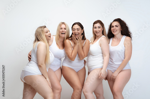 In love with myself. Portrait of beautiful plus size young women posing on white background. Happy smiling female models laughting together. Concept of body positive, beauty, fashion, style, feminism.