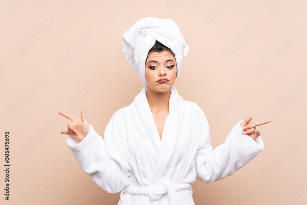 Teenager girl in a bathrobe over isolated background pointing to the laterals having doubts Teenager girl in a bathrobe over isolated background pointing to the laterals having doubts