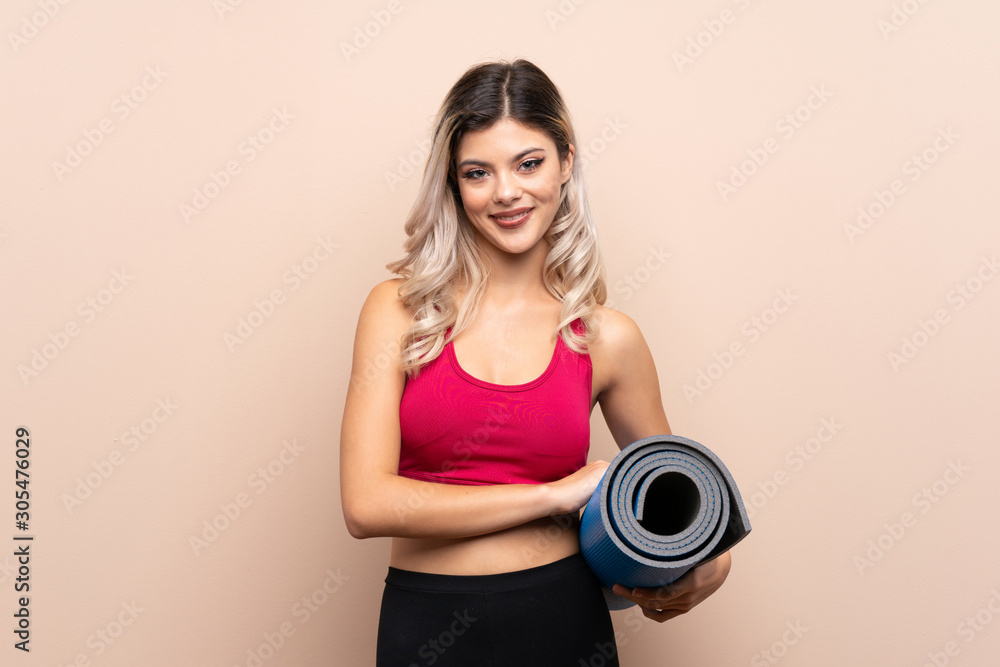 Teenager sport girl over isolated background with a mat and smiling Teenager sport girl over isolated background with a mat and smiling