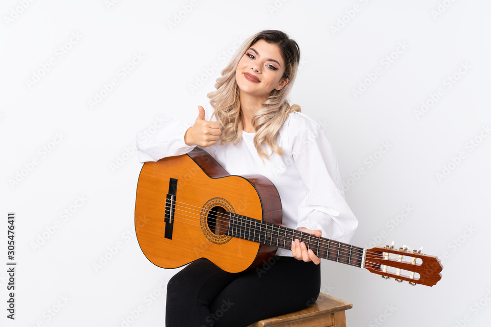 Teenager girl with guitar over isolated white background with thumbs up because something good has happened Teenager girl with guitar over isolated white background with thumbs up because something good has happened