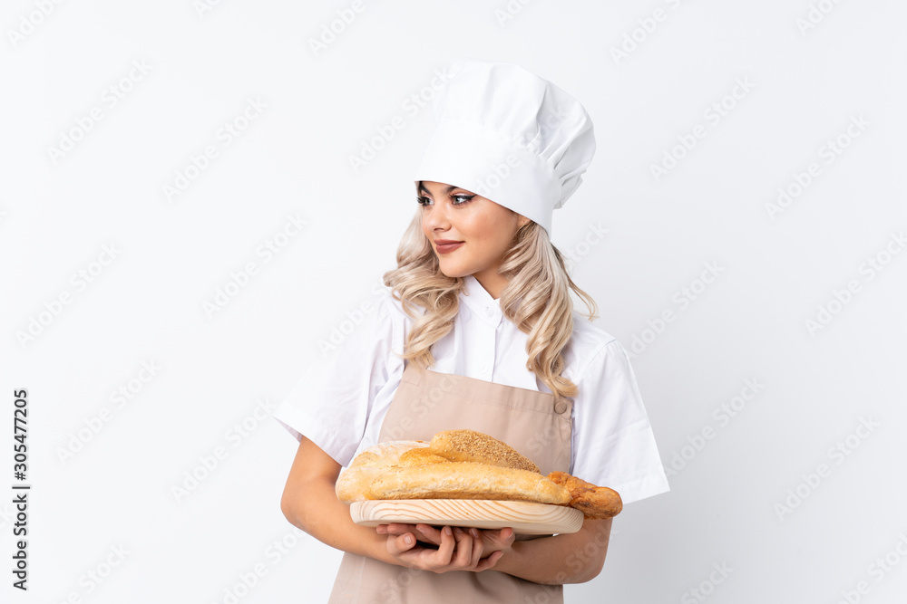 Teenager girl in chef uniform. Female baker holding a table with several breads over isolated white background looking to the side Teenager girl in chef uniform. Female baker holding a table with several breads over isolated white background looking to the side