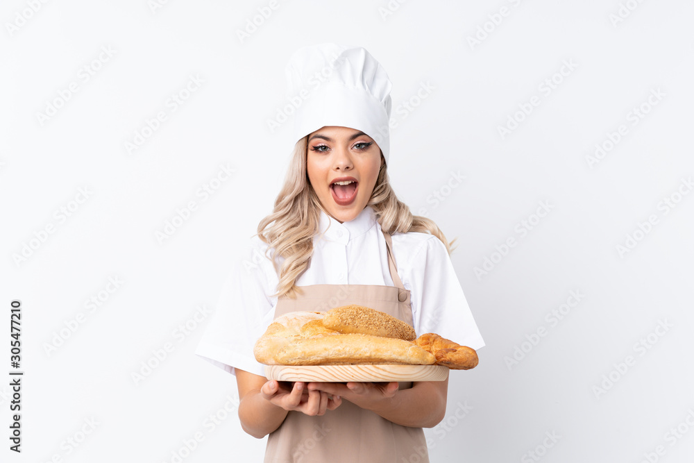 Teenager girl in chef uniform. Female baker holding a table with several breads over isolated white background with surprise facial expression Teenager girl in chef uniform. Female baker holding a table with several breads over isolated white background with surprise facial expression