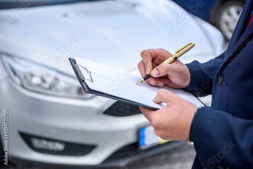 Male hands with clipboard against new car