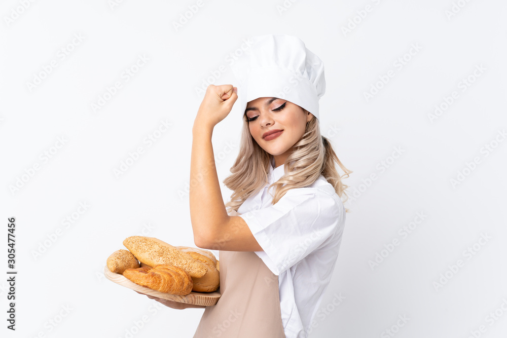 Teenager girl in chef uniform. Female baker holding a table with several breads over isolated white background making strong gesture Teenager girl in chef uniform. Female baker holding a table with several breads over isolated white background making strong gesture