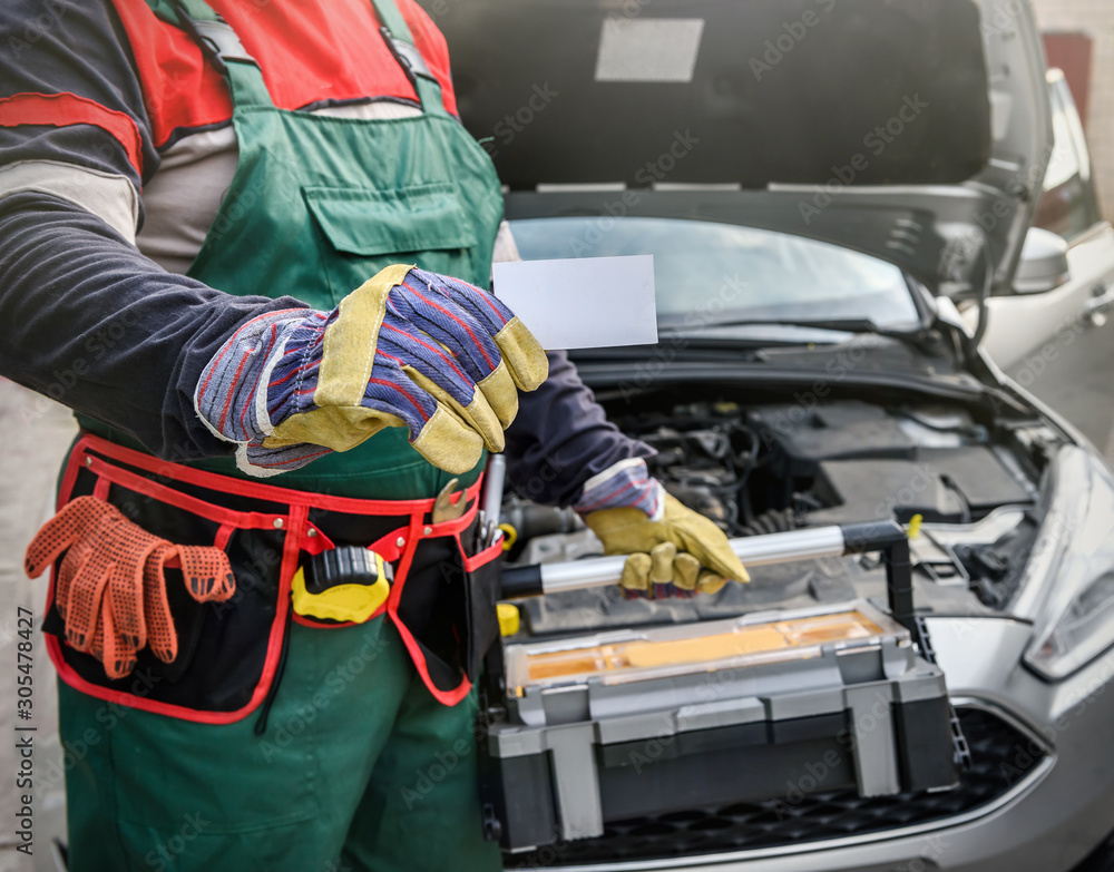 Mechanic with tool box and car with opened hood showing visit card Mechanic with tool box and car with opened hood showing visit card