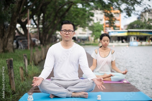 Young couple is doing yoga  with the garden as background. Concept of  healthy.