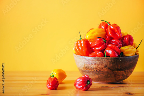 Yellow and red scotch bonnet chili peppers in wooden bowl over orange background. Copy space.