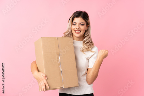 Teenager girl over isolated pink background holding a box to move it to another site © luismolinero