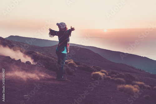 Happy traveler woman viewed from back opening arms to hug the wonderful awesome nature during sunset time - enjoying the world and wanderlust lifetyle people - coloured jacket - happy travel people 