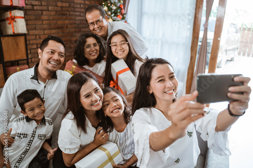 asian family wearing white take selfie using smartphone together at home on christmas day