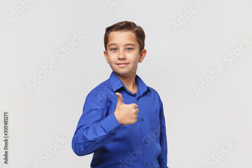 Smiling young boy in blue classic shirt shows thumbs up