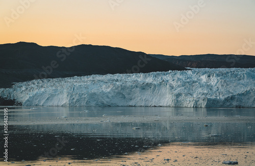 Greenland glacier nature landscape with famous Eqi glacier and lodge cabins. Midnight sun and pink sky. Tourist destination Eqi glacier in West Greenland AKA Ilulissat and Jakobshavn Glacier. Heavlly photo