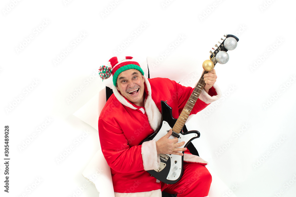 Santa Claus with an electric guitar from a hole in paper. Christmas Holidays. Man in a New Year's suit from the wall Santa Claus with an electric guitar from a hole in paper. Christmas Holidays. Man in a New Year's suit from the wall
