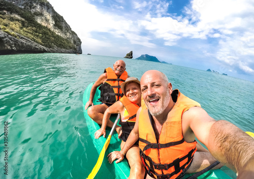 Senior mother and father with son taking selfie at kayak excursion in Thailand - Adventure travel in south east asia - Elderly and family concept of love sharing moments with parents - Warm vivid look