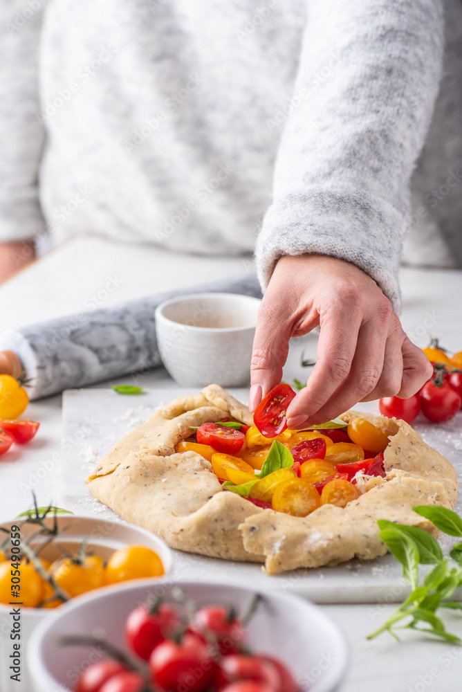 Women preparing tomatoes and basil galette on white table Women preparing tomatoes and basil galette on white table