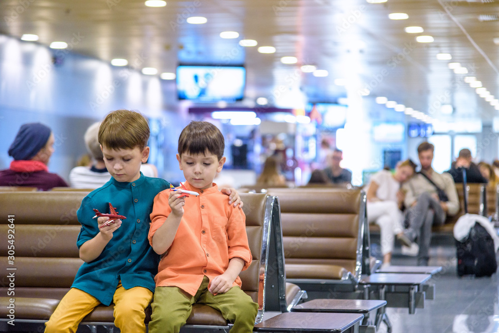 Two young brother boy dreaming of becoming a pilot. A child with a toy airplane plays at airport waiting for departure on their aircraft. Travel and holidays with children concept