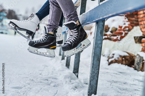 Couple wearing ice skates sitting on a guardrail photo