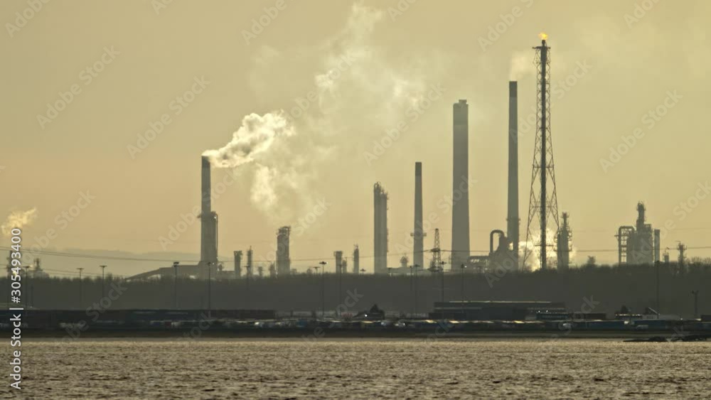 Industrial estuary land and seascape. Showing buildings in silhouette with high lit pollutant steam and smoke. Industrial estuary land and seascape. Showing buildings in silhouette with high lit pollutant steam and smoke.