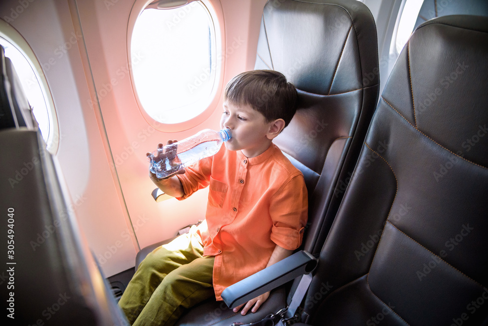 Charming kid traveling by an airplane. Little boy drinking water during the flight. Air travel with little kids Charming kid traveling by an airplane. Little boy drinking water during the flight. Air travel with little kids