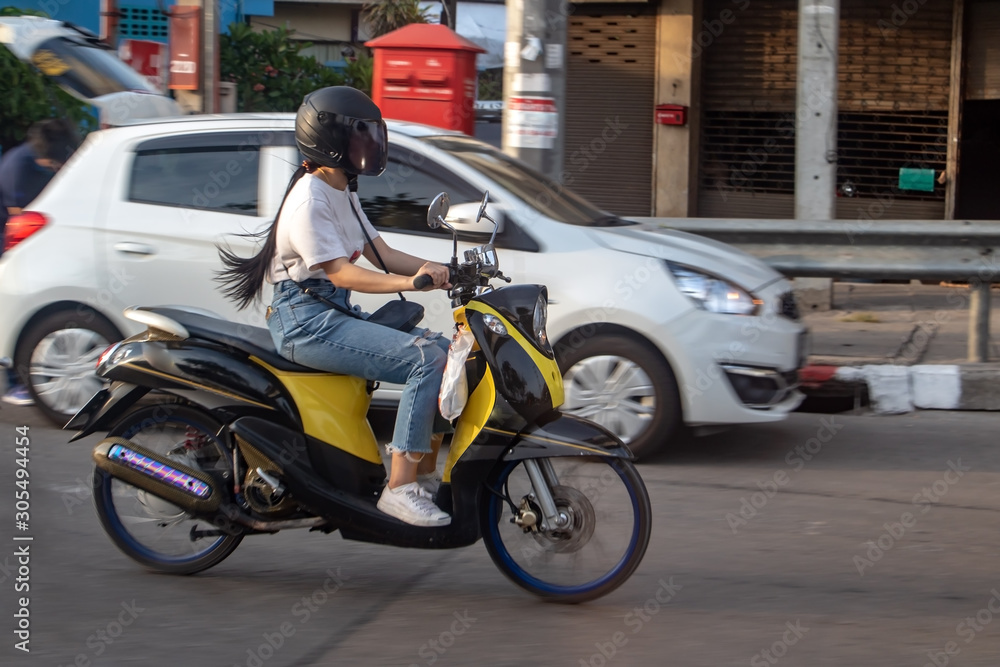 A young woman riding a motorcycle on road. Asian girl rides scooter in the city street, Samut Prakan, Thailand.